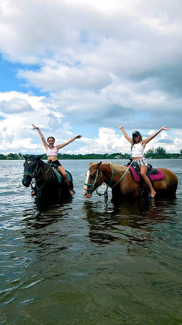 Kendra and her daughter on horseback in the shallow water, arms raised