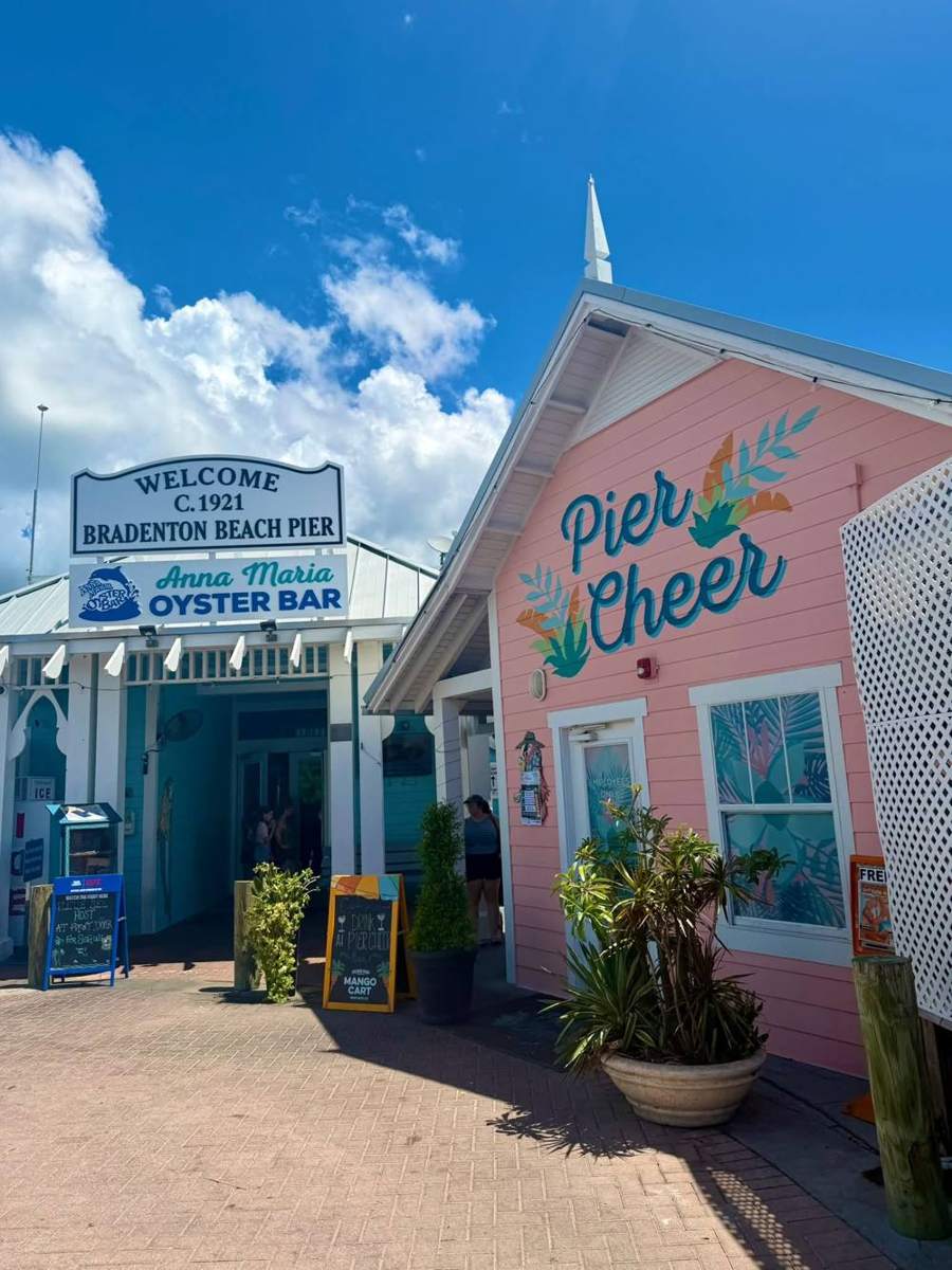 Welcome sign for the Bradenton Beach Pier with Anna Maria Oyster Bar and the pink Pier Cheer bar