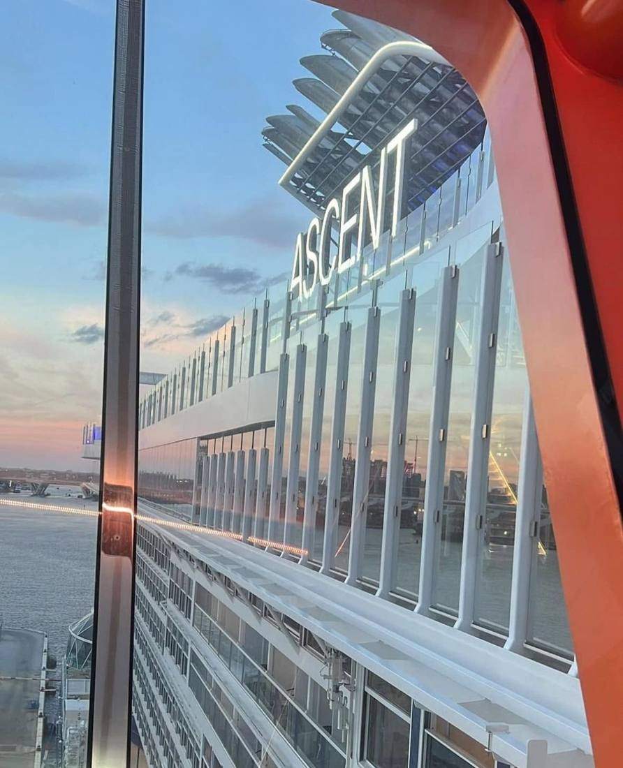 The Celebrity Ascent name glowing at sunset, seen through a window