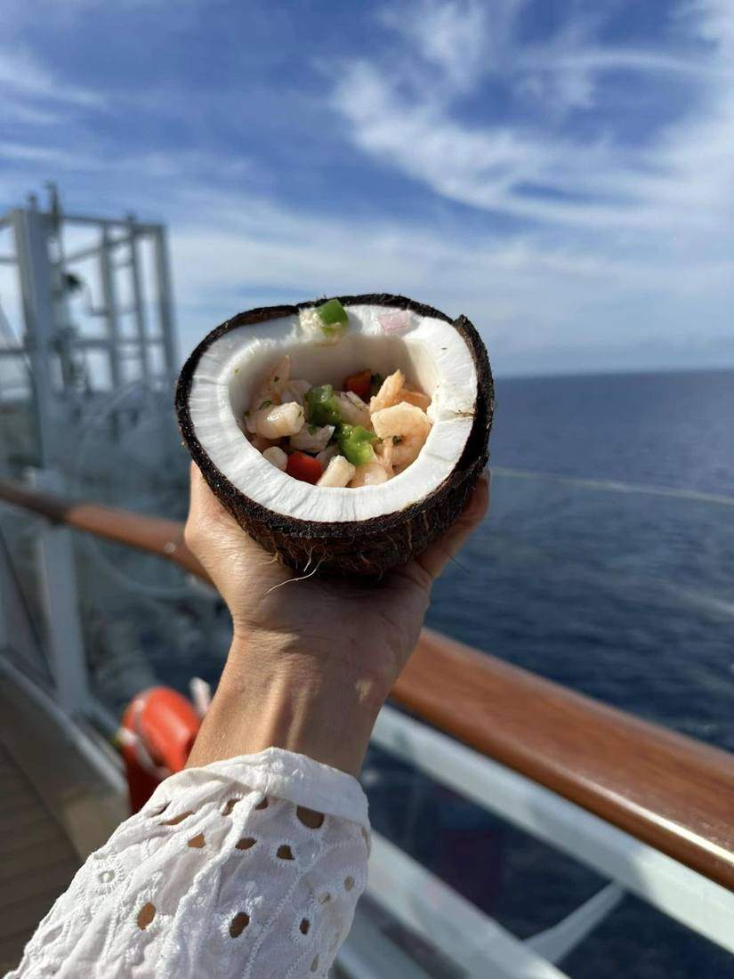 Shrimp ceviche served in a coconut shell held over the ocean