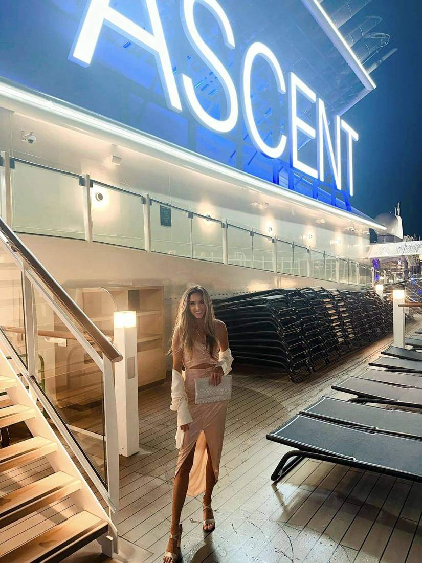 Kendra standing under the glowing Ascent sign at night