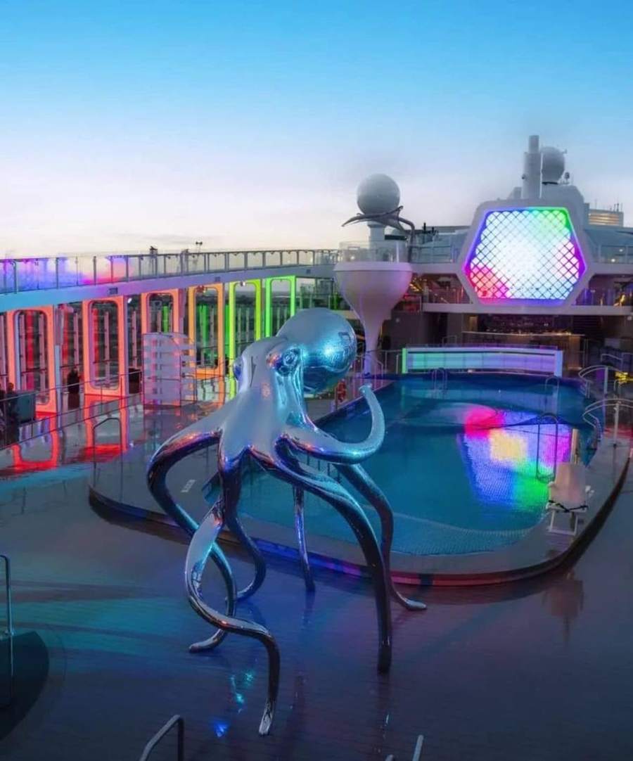 A mirrored octopus sculpture beside a lit-up pool at dusk