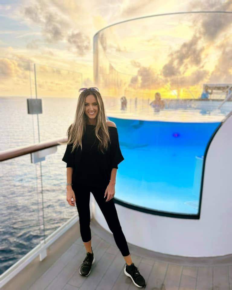 Kendra smiling beside a glass-sided pool at sunset