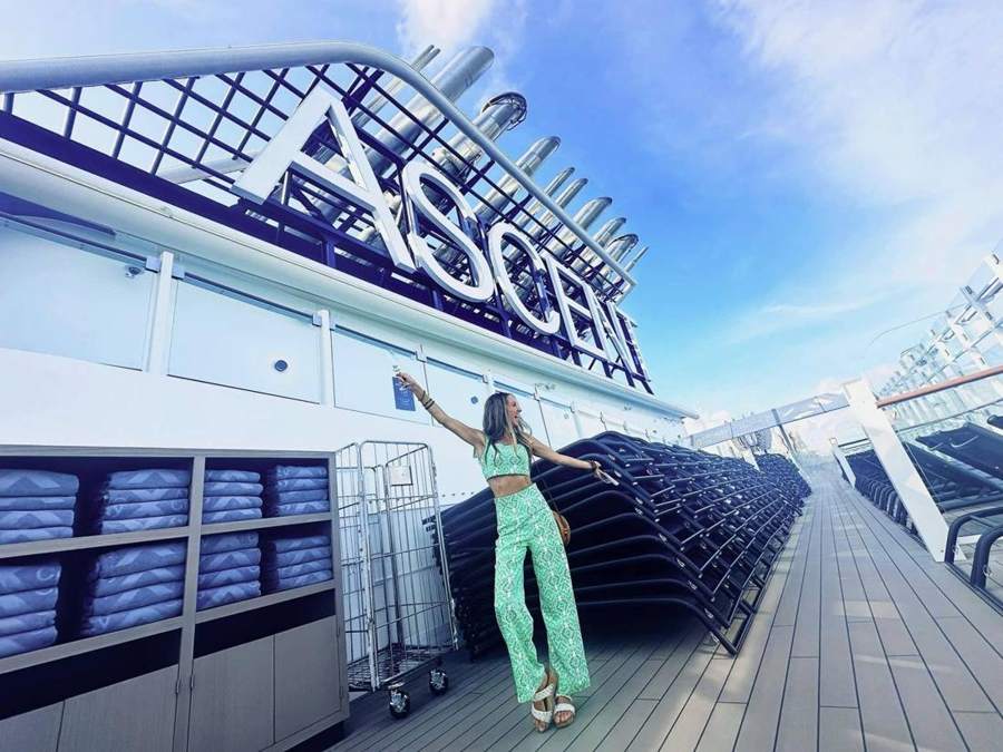 Kendra raising a glass under the Celebrity Ascent sign on the pool deck