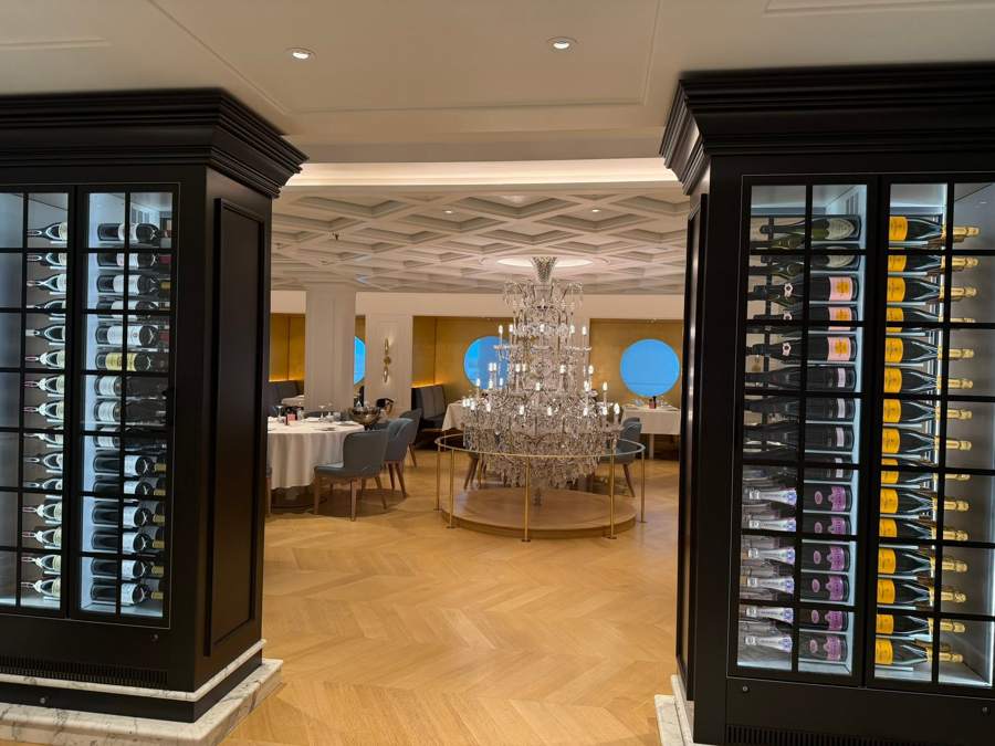 A dining room with a crystal chandelier between two wine display cases