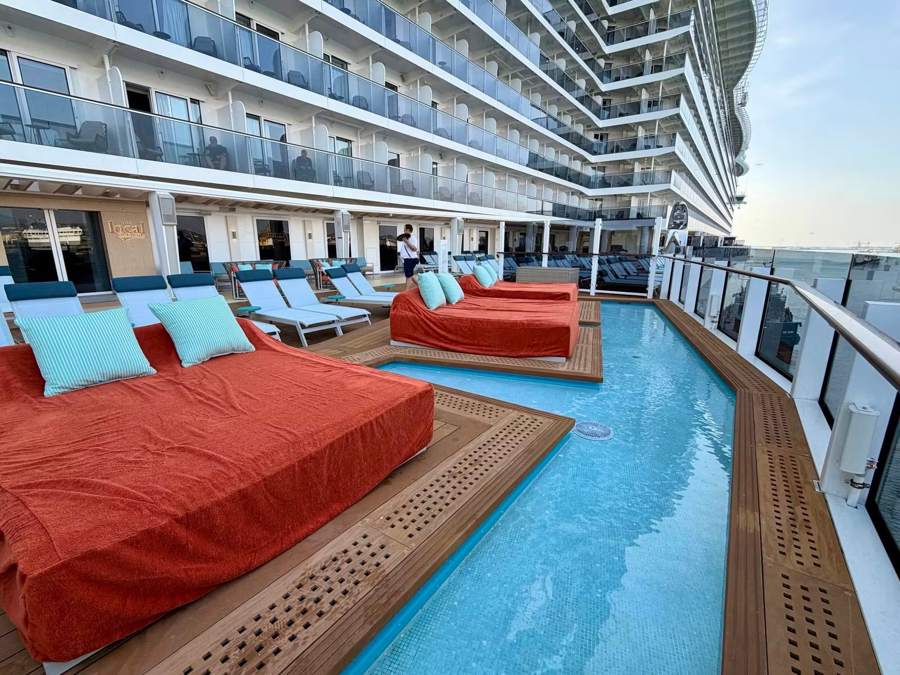 Orange daybeds beside a narrow plunge pool along the side of the ship