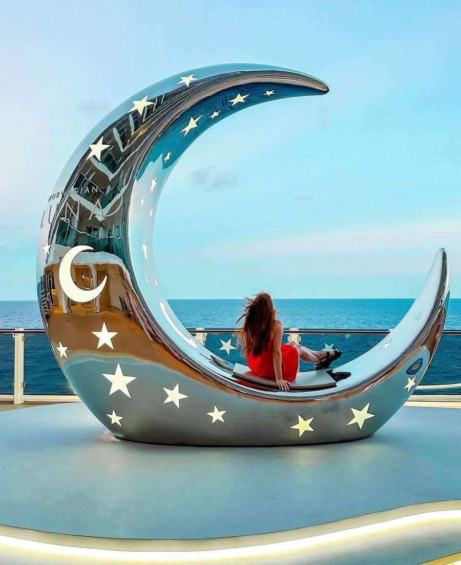 A mirrored crescent moon seat on deck with a woman sitting in it facing the ocean