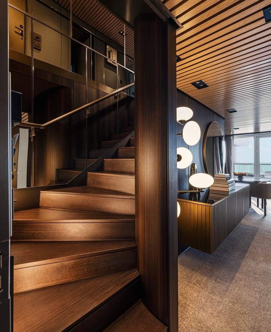 A wood-paneled suite stairwell with round wall lights and an ocean view