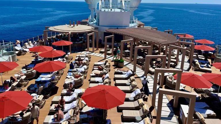 Sun loungers and red umbrellas on a ship deck over blue ocean